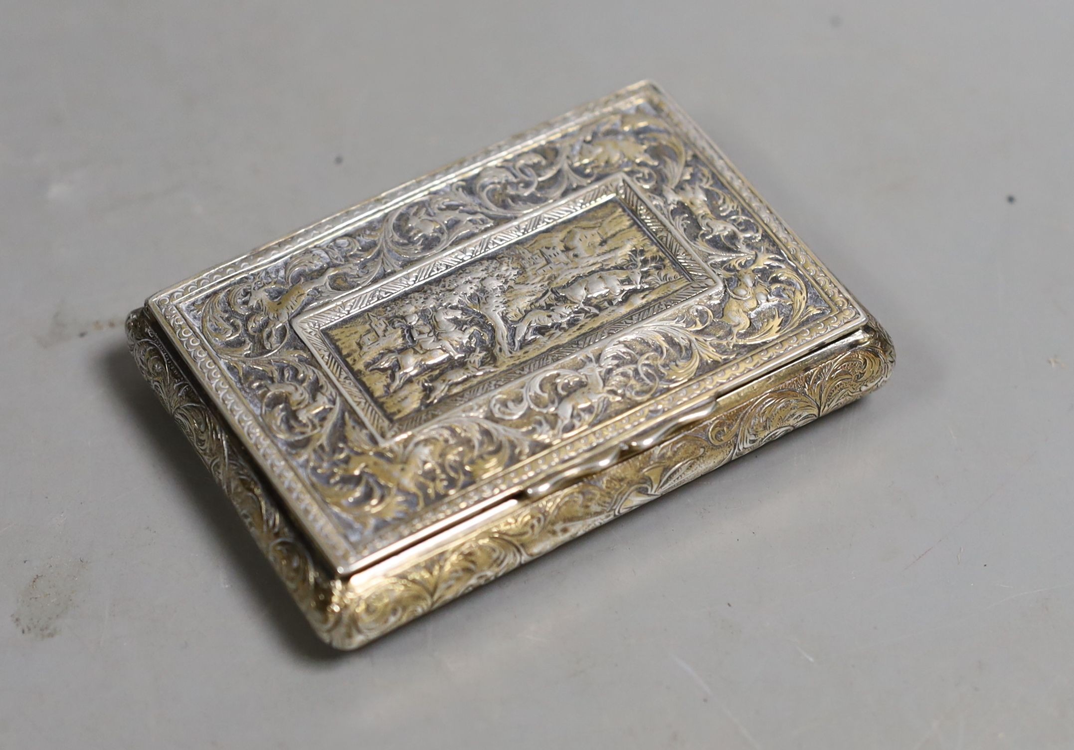 A 19th century continental gilt white metal rectangular bombe shaped snuff box, embossed with foliate scrolls and central stag hunting scene, unmarked, 81mm.